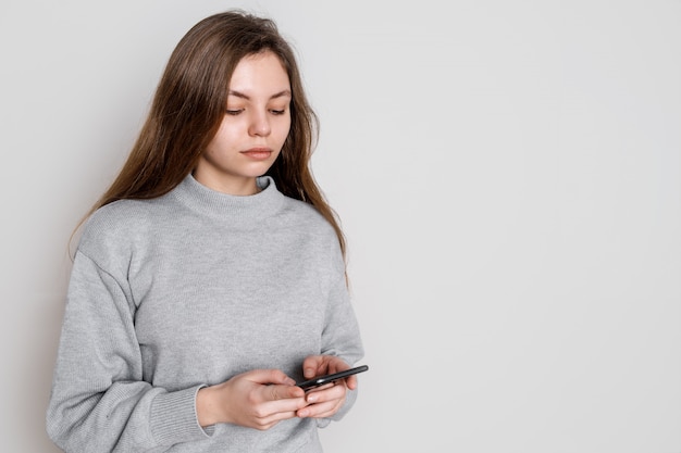 Rozochocona młoda kobieta używa smartphone w studiu na białym tle. Millenial concept. Media społecznościowe
