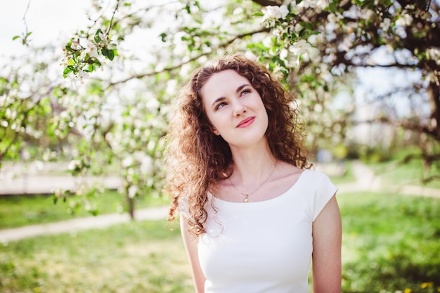 Rozochocona młoda kobieta w białej koszulce pod kwitnącym drzewem.