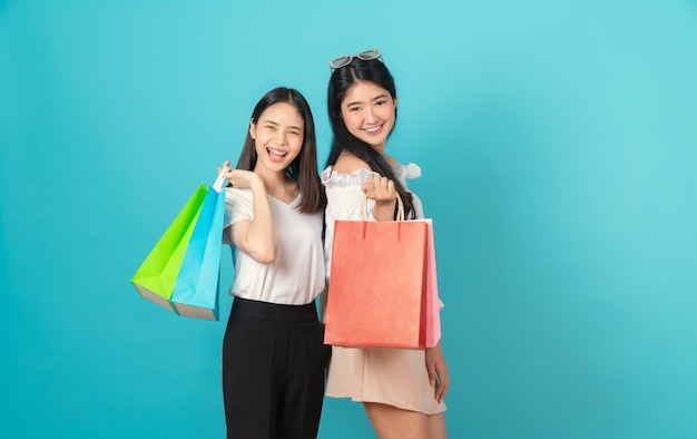 Rozochocona piękna dwa Azjatycka kobieta trzyma wielo- barwionych torba na zakupy na bławej ścianie