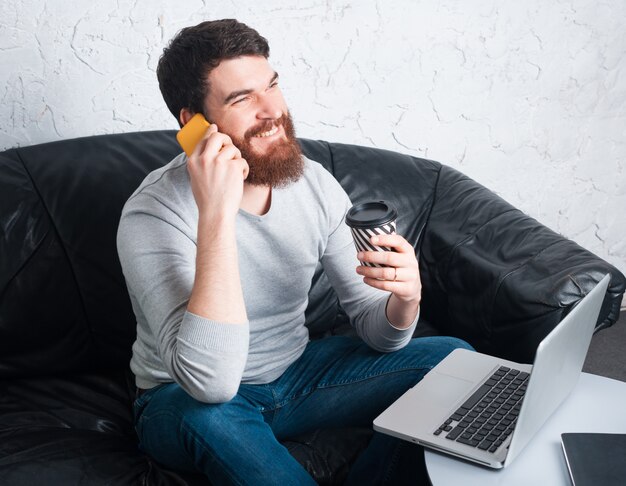 Rozochocony mężczyzna z brody obsiadaniem w biurze i opowiadać na smartphone