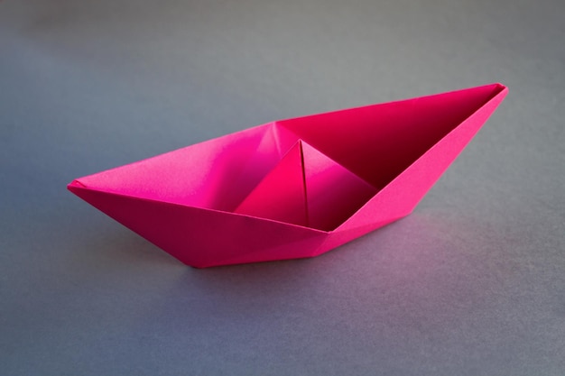 Różowa papierowa łódź origami na białym tle na szarym tle