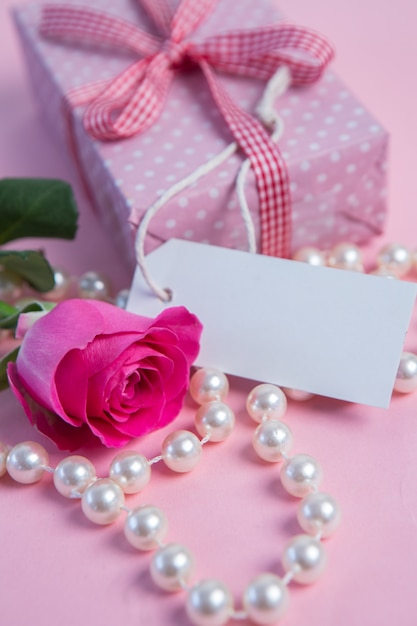 Różowa róża z prezentem i sznur pereł z pustą etykietą