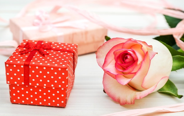 Zdjęcie różowa róża z pudełkami na prezent na białym drewnianym stole z bliska
