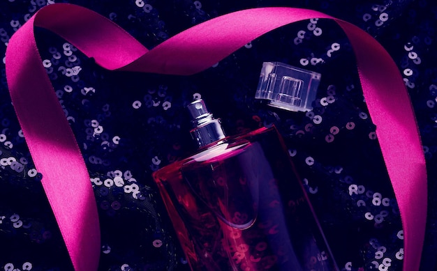 Zdjęcie różowa szklana butelka z różowym płynem perfumowym na czarnym tle z błyszczącymi pałeczkami z góry