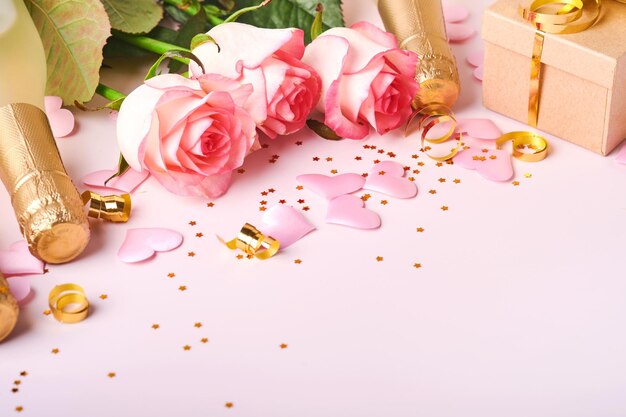 Różowe kwiaty róż, szampan, prezent, złote wstążki i konfetti czerwone serca na różowym tle. Płaski widok z góry z miejscem na pozdrowienia. Walentynki tło i kartkę z życzeniami.