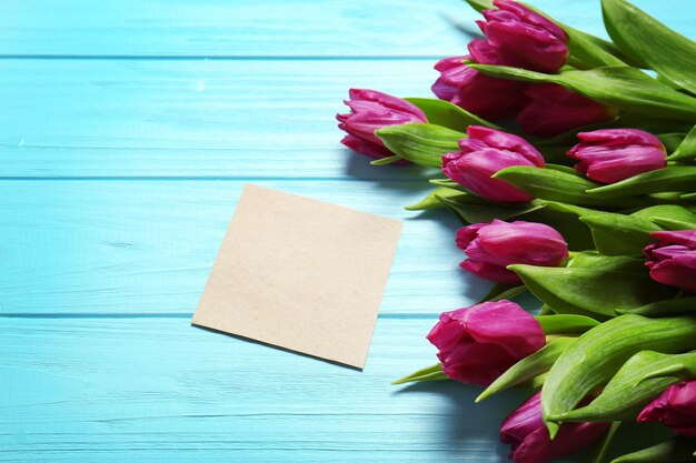 Różowe piękne tulipany z kartą z życzeniami na niebieskim drewnianym tle