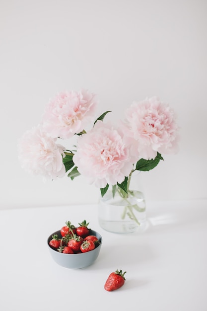 Różowe piwonie w wazonie i truskawki na stole