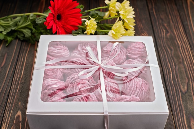 Zdjęcie różowe ptasie mleczko, zapakowane w pudełko ze wstążką i kwiatami, na prezent, na drewnianej desce