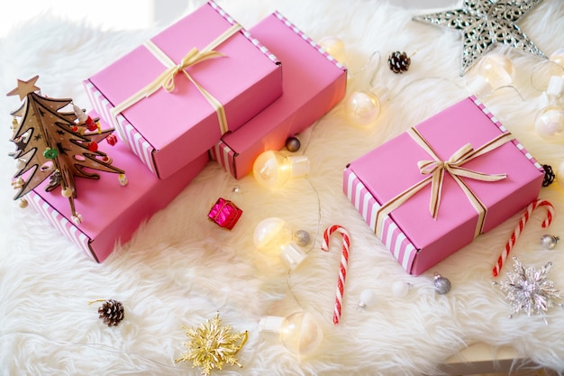 Różowe pudełka na prezenty z zamkniętą wstążką z kokardką z jasną lampą, cukierkami i gwiazdą na białym dywanie do świętowania