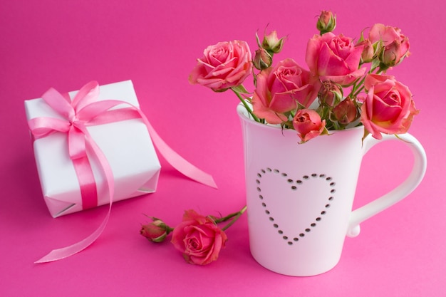 Różowe róże w białej filiżance i prezent