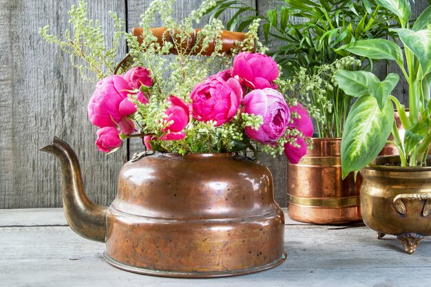 Zdjęcie różowe róże w starym mosiężnym czajniku i zielonych roślinach