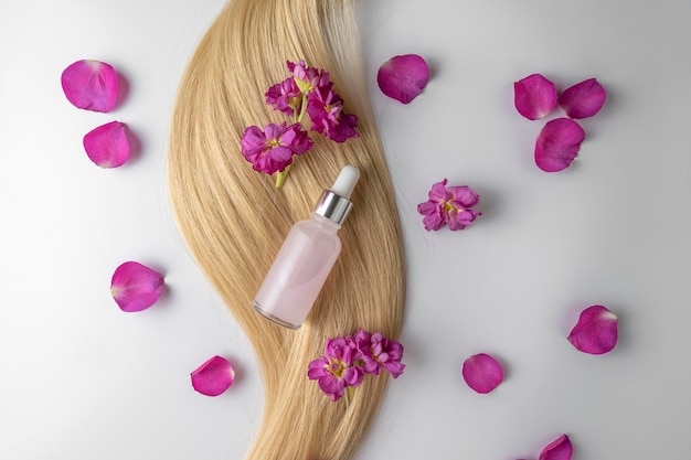 Różowe serum lub olejek do twarzy z płatków róż z ekstraktem z kwiatów leżących na kosmyku blond włosów makieta marketingowa produktu Koncepcja pielęgnacji włosów w salonie lub w domu