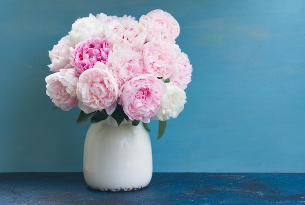 Różowe świeże różowe kwiaty piwonii w wazonie na niebieskim tle z miejscem na kopię