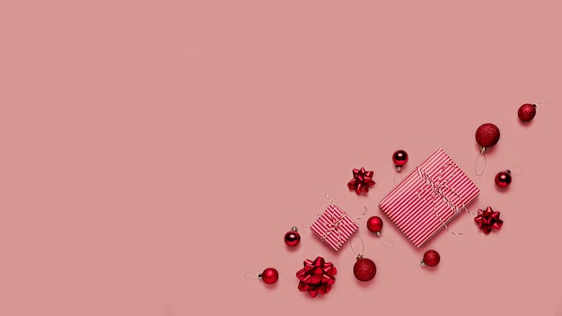 Różowe tło z różowym prezentem świątecznym prezentem, małe czerwone bombki lub zabawki kuli, wstążki kokardki na choinkę, inne ozdoby. Świąteczne wyprzedaże, zakupy lub kartka z życzeniami lub zaproszenie
