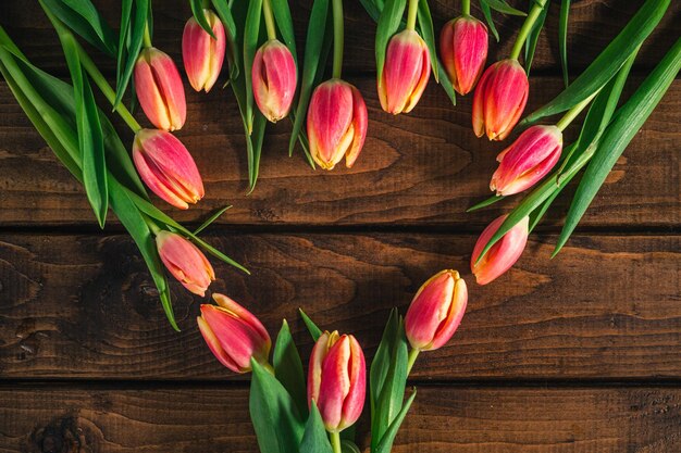 Różowe tulipany leżą na drewnianym stole w kształcie serca