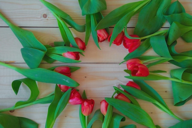 Różowe tulipany z zielonymi liśćmi leżą w okręgu z wolnym miejscem pośrodku na drewnianym tle