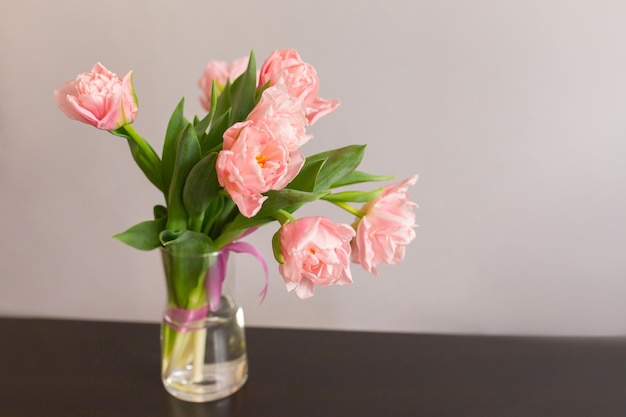 Różowe tulipany z zielonymi liśćmi w szklanym wazonie na stole Miejsce na tekst