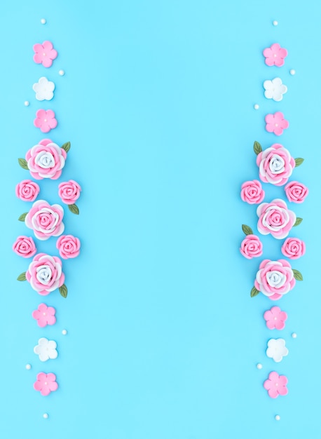 Różowo-białe kwiaty wykonane z pianiranu z zielonymi liśćmi i białymi koralikami na niebieskim tle.
