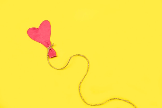 Różowy balon w kształcie serca opróżniony z włóczki sizalowej na żółtym tle z miejscem na kopię