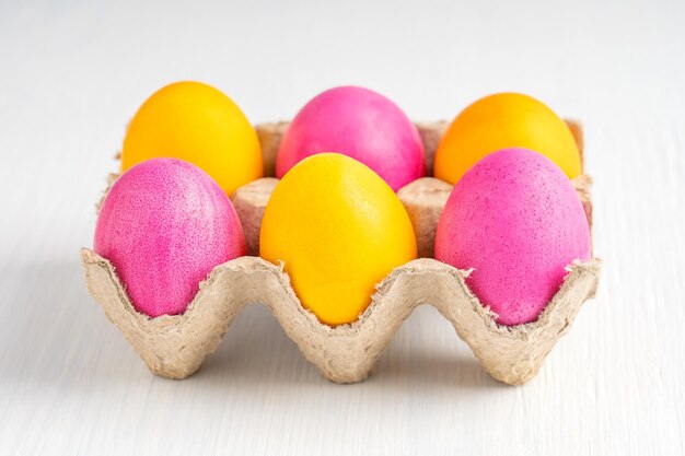 Różowy i żółty karton na jajka wielkanocne z różowymi i żółtymi jajkami na białym stole