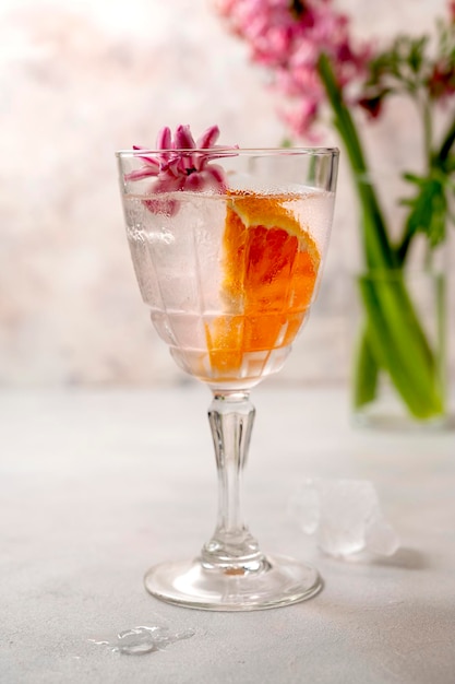 Różowy koktajl z plasterkiem pomarańczy i kostkami lodu w kryształowych szklankach z różowymi wiosennymi kwiatami Hiacynt Alkoholowy orzeźwiający napój imprezowy