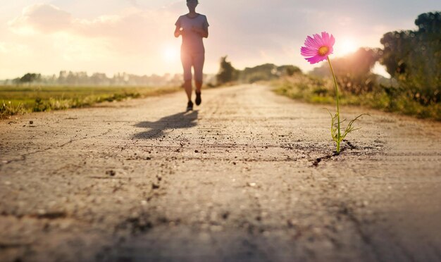 Różowy kwiat rosnący na pękniętej ulicy, a kobieta biega i biega po wiejskiej drodze