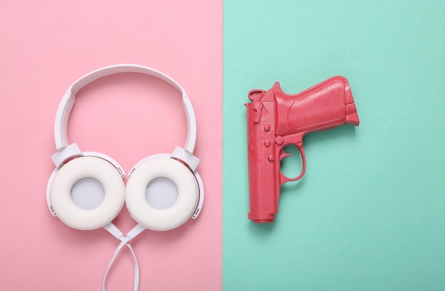Różowy pistolet pistoletowy ze słuchawkami na niebieskim różowym tle Koncepcja kreatywna Minimalizm Płaski układ Minimalny układ Widok z góry