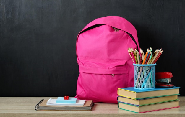 Różowy plecak i przybory szkolne na stole na czarnym tle