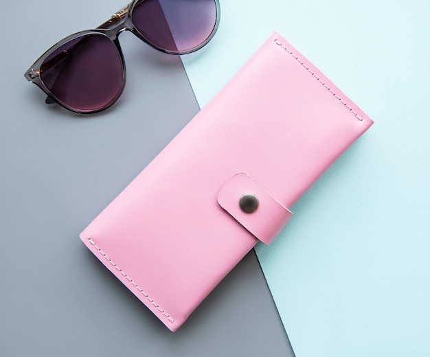 Różowy skórzany portfel i okulary przeciwsłoneczne na szaro-zielonej powierzchni