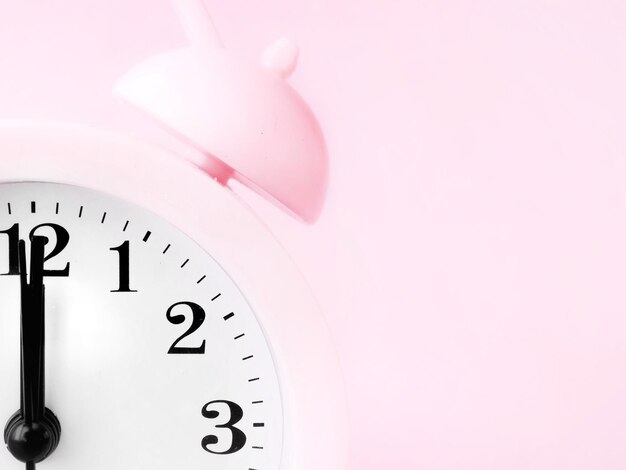 Różowy zegar budzik o 12 rano o 12 po południu izolowany na różowym tle przestrzeń do kopiowania
