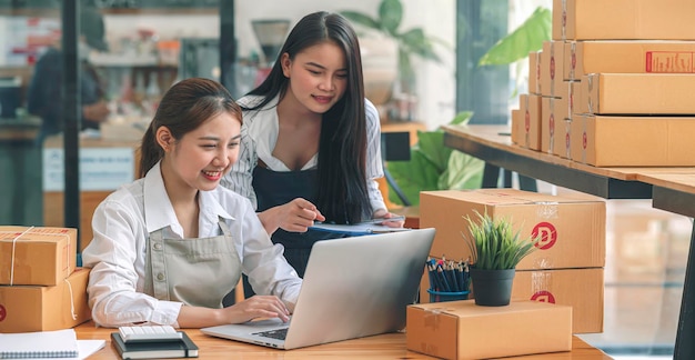 Rozpoczęcie małych firm MŚP. Piękna azjatycka przedsiębiorca i jej koleżanka za pomocą laptopa sprawdzają zamówienie online i przygotowują się do pakowania dla klienta. Pomyślna koncepcja online biznesu MŚP.