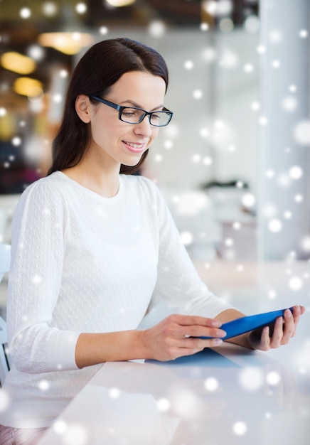 rozrywka, biznes, ludzie, technologia i koncepcja stylu życia - uśmiechnięta młoda kobieta w okularach z komputerem typu tablet pc w kawiarni nad efektem śniegu