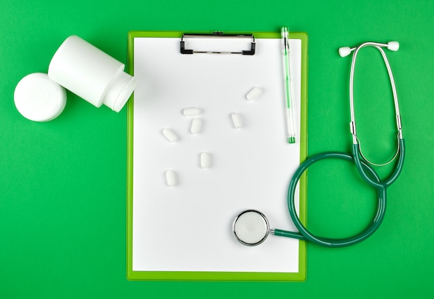Rozrzucone białe owalne tabletki z plastikowego słoika, stetoskop