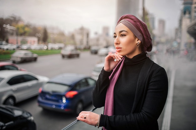 Zdjęcie rozważna młoda arabska kobieta stoi przy krawędzią i patrzeje drogę z samochodami.