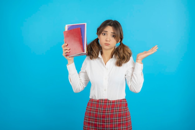 Rozważna Studentka Trzyma Jej Książki I Stoją Na Niebieskim Tle. Zdjęcie Wysokiej Jakości