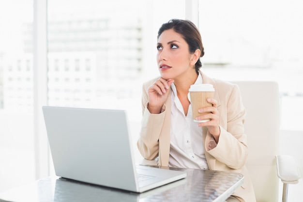 Rozważny bizneswoman pije kawę podczas gdy pracujący na laptopie
