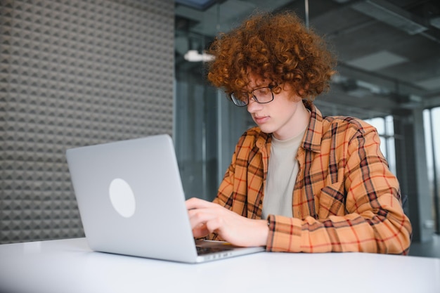 Rozważny freelancer w zwykłych ubraniach przeglądający laptopa podczas pracy nad projektem na tarasie kawiarni w ciągu dnia