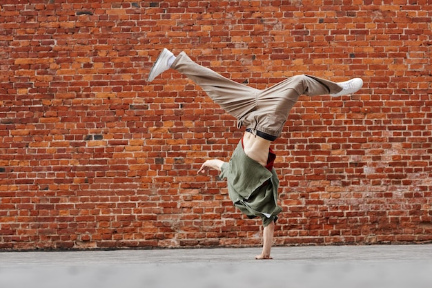 Ruch strzał młodego człowieka robi breakdance handstand poza przed ceglaną ścianą miejsca kopiowania