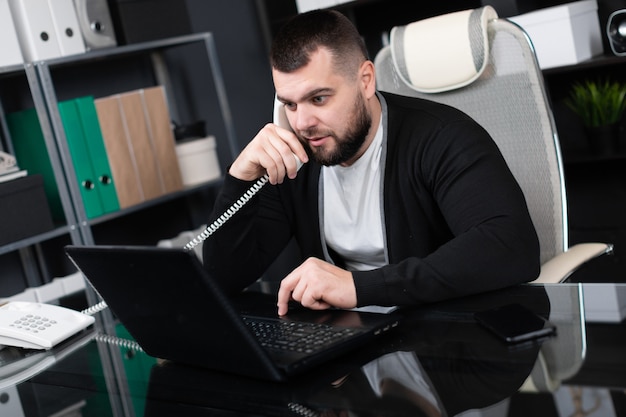 Ruchliwie młody człowiek opowiada telefon i patrzeje laptop w biurze