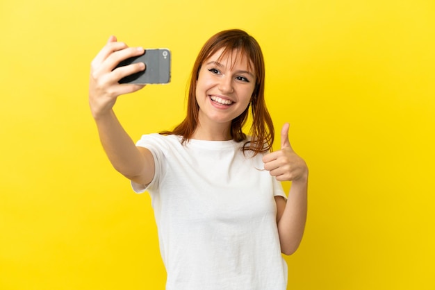 Ruda dziewczyna na żółtym tle robi selfie z telefonem komórkowym