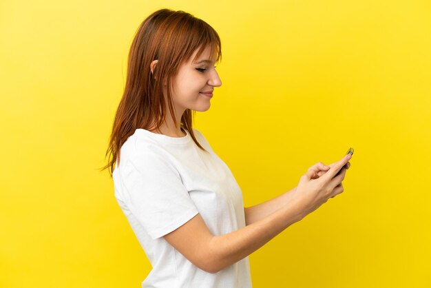 Ruda dziewczyna odizolowana na żółtym tle wysyłająca wiadomość lub e-mail za pomocą telefonu komórkowego