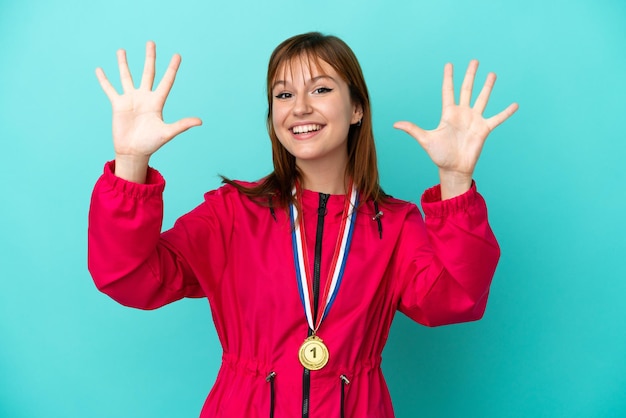 Ruda dziewczyna z medalami na białym tle na niebieskim tle, licząc dziesięć palcami