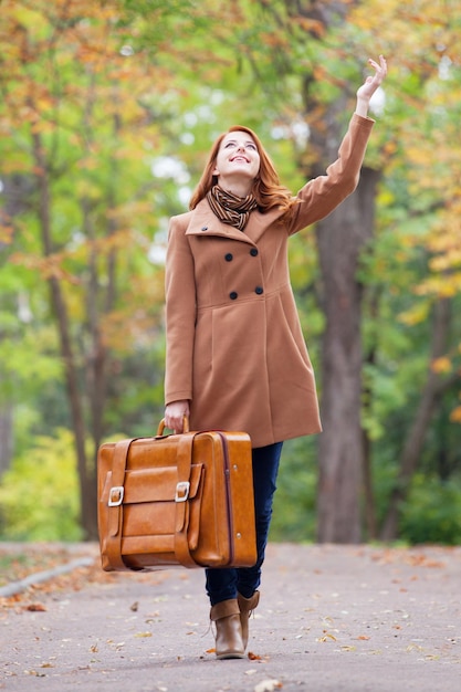 Ruda dziewczyna z walizką na jesień na świeżym powietrzu