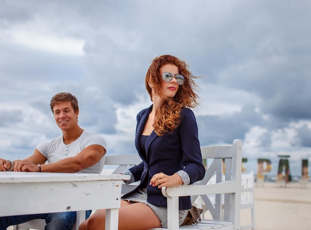 Ruda kobieta i jeden facet siedzący przy stole na plaży.