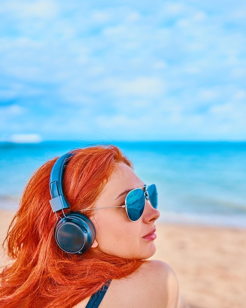 Ruda kobieta słucha muzyki na plaży seksowna kobieta słucha muzyki na plaży con...