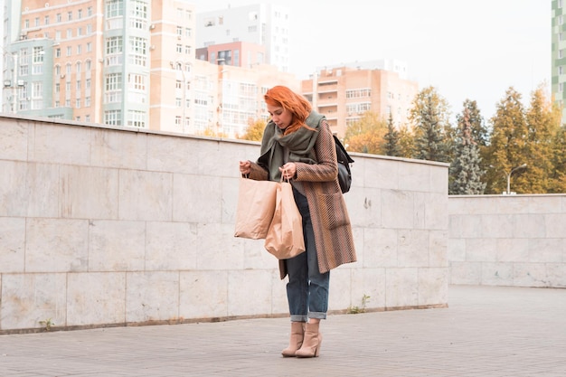 Ruda kobieta w jesiennym stroju z dużymi papierowymi torbami na zakupy w mieście
