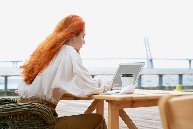 Ruda kobieta wpisując na laptopie w kawiarni na świeżym powietrzu