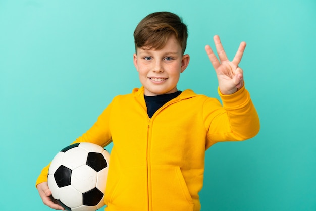 Rude dzieciak grający w piłkę nożną na białym tle na niebieskim tle szczęśliwy i liczący trzy palcami