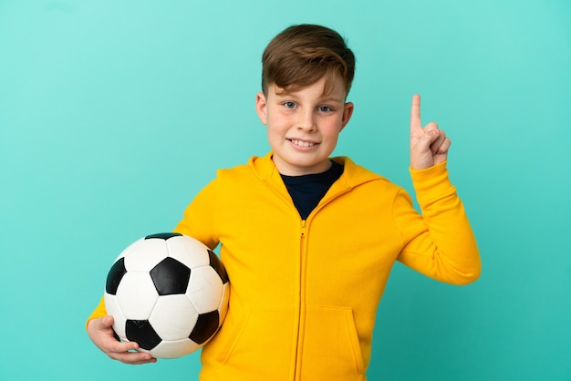 Rude dziecko grające w piłkę nożną izolowane na niebieskiej powierzchni, wskazując na świetny pomysł