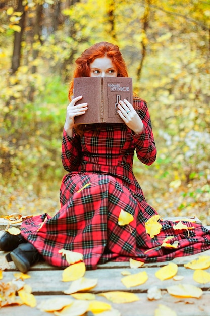 Zdjęcie rude dziewczyny w czerwonej sukience, kapelusz spaceru w jesiennym lesie. szczęśliwy styl życia. jesień. żółte liście